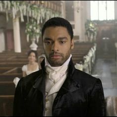 a man in a black suit and white shirt standing in front of pews at a church