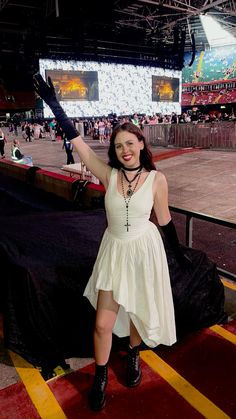 a woman in a white dress and black boots posing for the camera at a concert