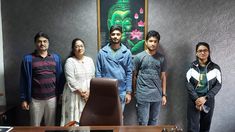 four people standing in front of a desk with a painting on the wall behind them