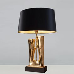 a table lamp with a black shade on it and a gold sculpture in the middle