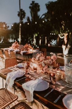 an outdoor dining table set up with flowers and place settings for guests to sit at