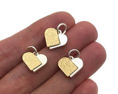 two pieces of gold and silver heart shaped pendants on a person's hand