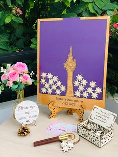 a table topped with lots of assorted items and flowers next to a purple card