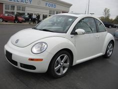 a white volkswagen beetle parked in front of a dealership with people standing around it