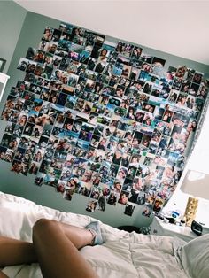 a woman laying on top of a bed in front of a wall with pictures all over it