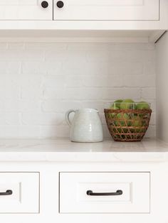 a basket with apples sitting on top of a white counter next to a wall mounted oven