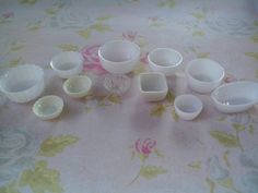 a table topped with lots of white bowls and cups on top of a floral covered table cloth