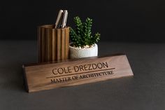 a wooden desk sign with a plant and pen holder on it's side that says cole drezdon master of architecture