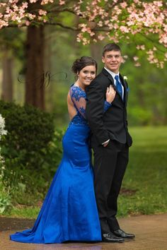 a young man and woman in formal wear posing for a photo under a flowering tree