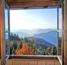 an open window with the view of mountains and trees in fall colors from inside a wooden cabin