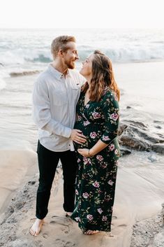 an engaged couple standing on the beach in front of the ocean