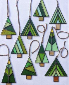 twelve stained glass christmas trees hanging from strings on a white surface with string attached to each ornament