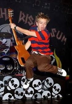 a young man jumping on top of a stage with a guitar in front of him