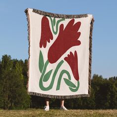 a woman standing in front of a large red and green flowered blanket on top of a grass covered field