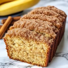 slices of cinnamon coffee cake on a marble surface with bananas and cinnamon sticks in the background