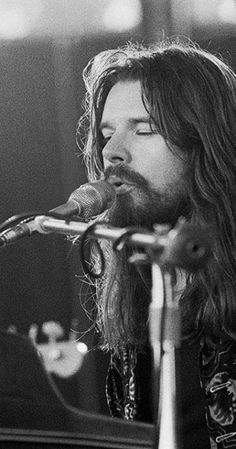 a man with long hair is singing into a microphone while playing the piano in front of him