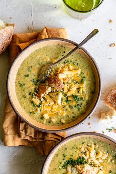 two bowls of broccoli soup on a table with bread and a glass of green juice