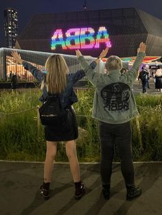 two people standing next to each other in front of a building with lights on it