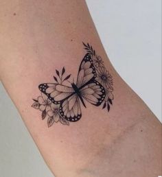 a black and white butterfly tattoo on the right side of the arm with flowers around it