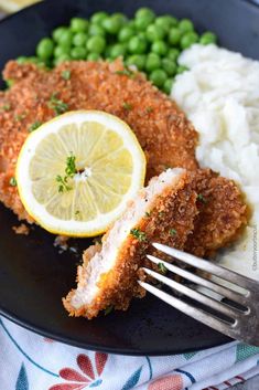 a plate with chicken, mashed potatoes, peas and lemon wedges on it