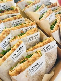 several sub sandwiches with labels on them sitting in a box