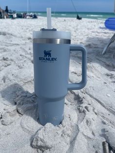 a travel mug sitting on the beach with a straw sticking out of it's handle