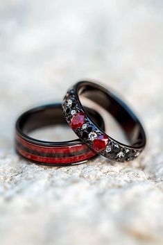 two wedding rings with red and black stones on them sitting on a white surface together