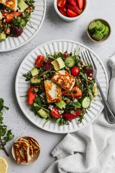 two plates filled with salad and fruit on top of a white tablecloth next to silverware