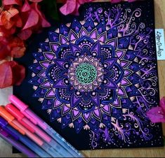 some markers and pens are sitting on a table next to a drawing book with an intricate design