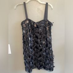 a black top with sequins hanging on a hanger next to a white wall