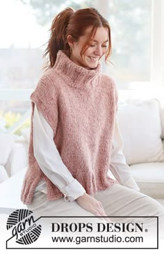 a woman sitting on top of a white couch wearing a pink knitted sweater and smiling