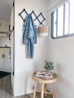 a coat rack with clothes hanging on it next to a stool and potted plant