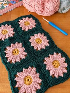 a crocheted granny blanket with pink and green flowers on it next to balls of yarn