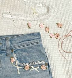 a pair of jeans with pink roses on them next to some scissors and laces