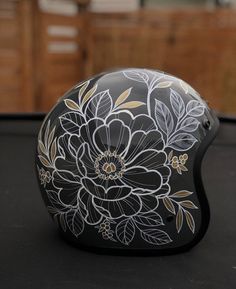 a motorcycle helmet with flowers painted on the side and gold foiled detailing, sitting on a black surface