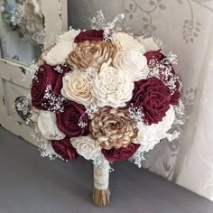 a bridal bouquet with red, white and beige flowers on a table in front of a mirror