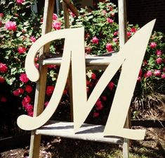 a wooden ladder with the letter m on it in front of some flowers and bushes