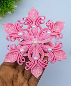 a hand holding a pink brooch with pearls on it's center and some flowers in the background