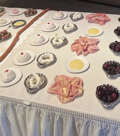 a table topped with plates and bowls filled with food next to a wooden spoon on top of a white table cloth