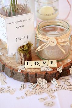 a table topped with a jar filled with flowers next to a wooden block that says love