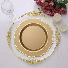 there is a gold plate on the table with flowers and wine glasses next to it