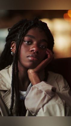 a woman with dreadlocks sitting in a chair looking off to the side and holding her hand on her chin