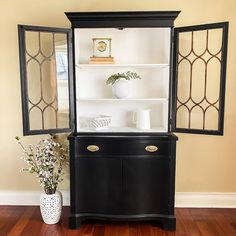 a black china cabinet sitting on top of a hard wood floor next to a vase with flowers