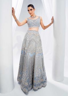 Indian Bridal Dress in Wedding Blue Choli Lehenga Style is a stunning attire adorned with hand-crafted details of embellishments. The alluring details of pearls, sequins, motifs, and embroidery make this beautiful Lehenga Choli dress an epitome of beauty and grace. Lehenga Choli: The choli in an alluring ice blue shade is intricately emblazoned with zardosi and hanging motifs. This choli in beautiful sleeveless style is adorned with shimmering silverwork, naqshi, tilla, beads, and sequins, makin Blue Embellished Sharara For Reception, Bollywood Style Embellished Ceremony Dress, Reception Traditional Wear With Pearl Embroidery, Traditional Reception Dress With Pearl Embroidery, Blue Sets With Pearl Embroidery For Reception, Anarkali-style Hand Embellished Lehenga For Ceremonies, Anarkali Hand Embellished Ceremony Dress, Embellished Anarkali Dress For Ceremony, Bollywood Style Embellished Gown For Ceremony