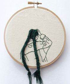 the embroidery is being worked on by someone who has just finished it and there are two green tassels hanging from the hoop