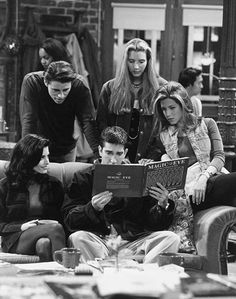 black and white photograph of four people sitting on a couch looking at an open book