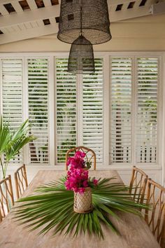 a dining room table with flowers on it and shuttered windows in the back ground