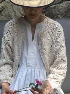 a woman wearing a white dress and hat holding a flower in one hand while sitting on a bench