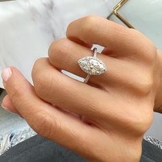 a woman's hand holding an engagement ring with a diamond center stone in the middle