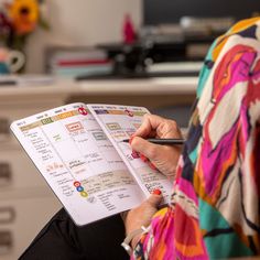 a woman sitting in a chair holding a pen and writing on a planner with her hand